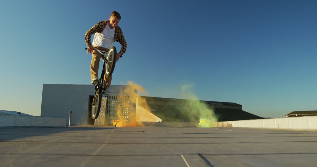 Man performing BMX bike stunt with colorful smoke on rooftop - Free Images, Stock Photos and Pictures on Pikwizard.com