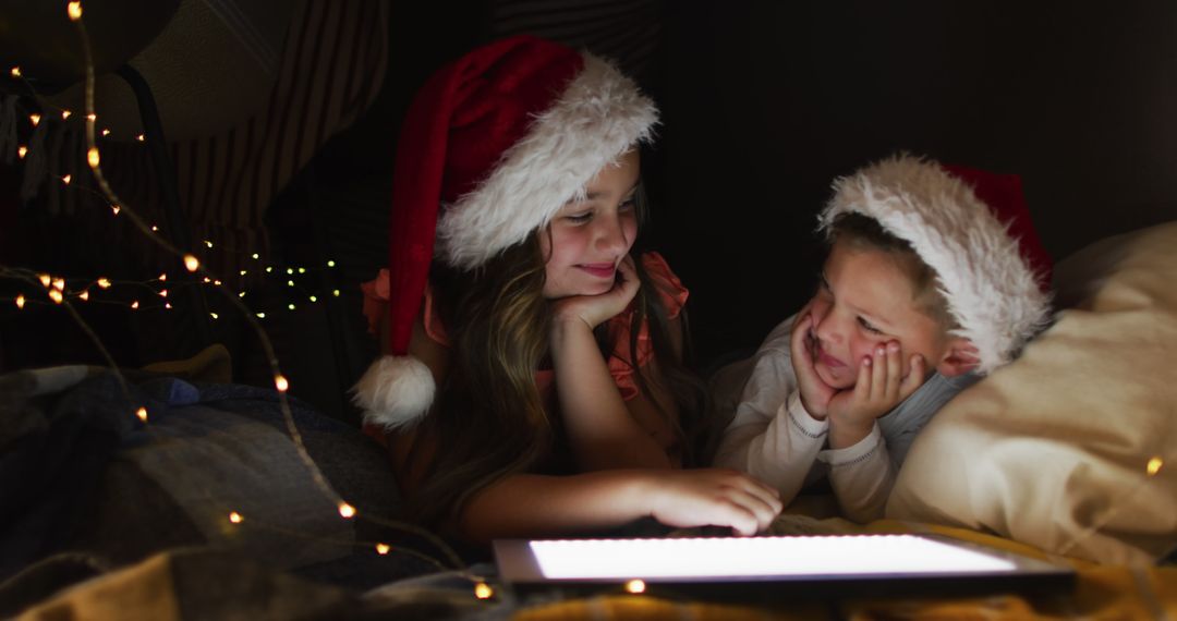 Children Wearing Santa Hats Using Tablet in Fort with Christmas Lights - Free Images, Stock Photos and Pictures on Pikwizard.com