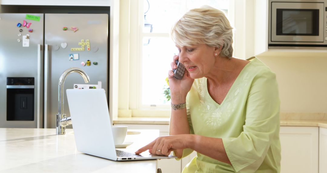 Senior Woman Talking on Phone and Using Laptop in Kitchen - Free Images, Stock Photos and Pictures on Pikwizard.com