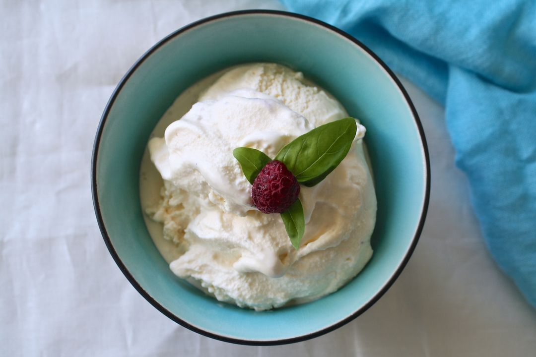 Creamy vanilla ice cream in turquoise bowl garnished with raspberry and fresh basil leaves