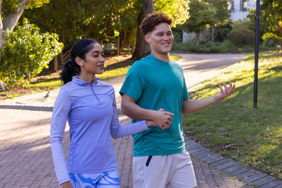 Diverse Couple Walking in Athletic Wear Holding Hands in Park