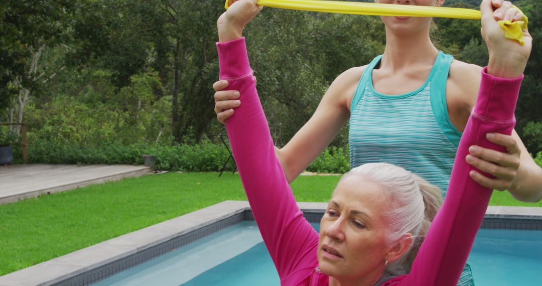 Personal Trainer Helps Woman with Resistance Band Exercise by Poolside