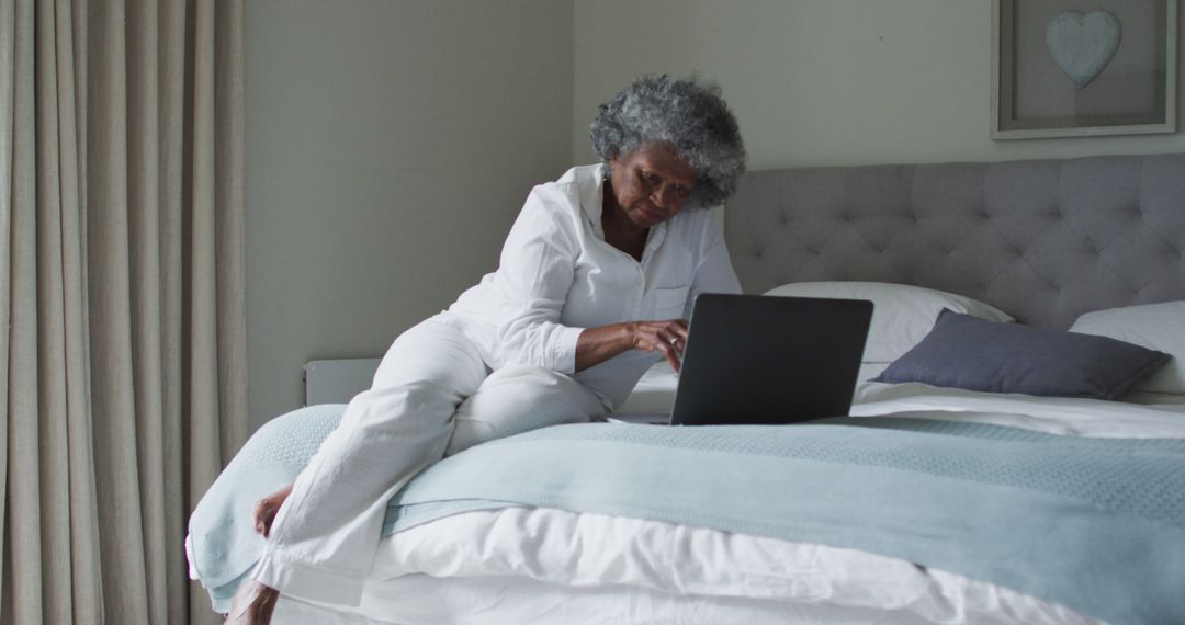 Elderly Woman in White Relaxing on Bed with Laptop at Home - Free Images, Stock Photos and Pictures on Pikwizard.com