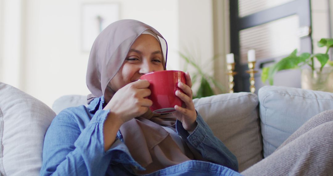 Smiling Muslim Woman Enjoying Warm Beverage on Cozy Couch - Free Images, Stock Photos and Pictures on Pikwizard.com