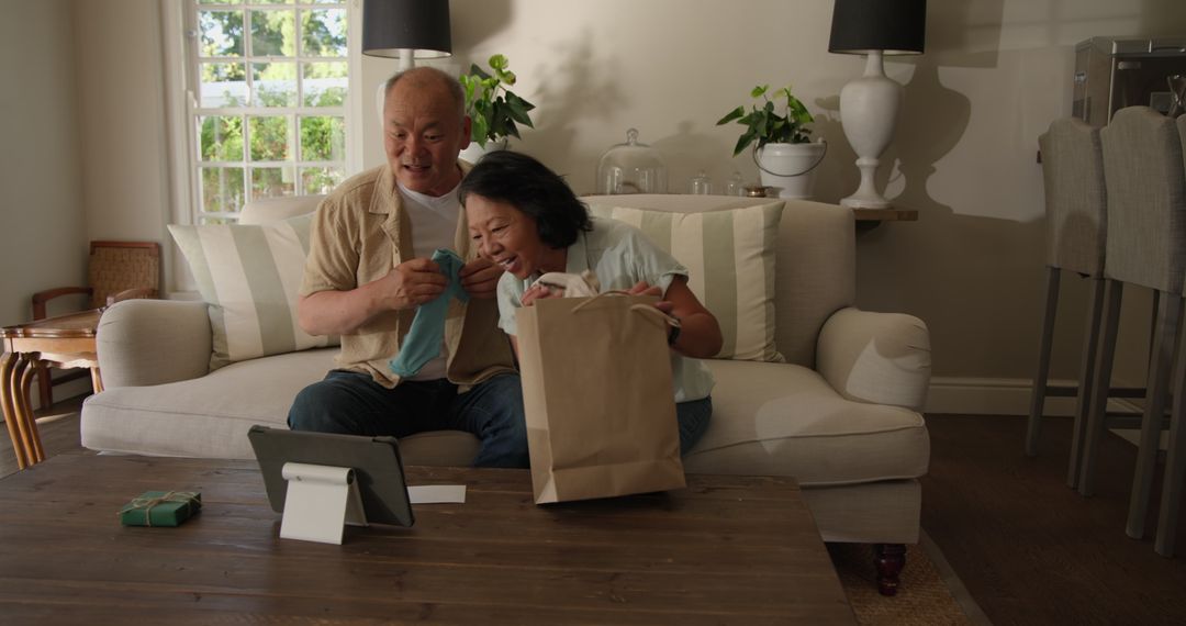 Smiling Elderly Couple Unboxing Gifts at Home on Sofa