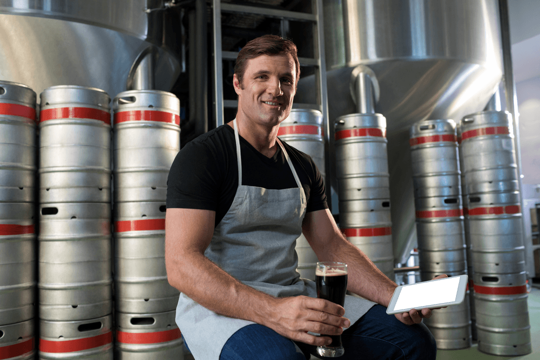 Portrait of Brewmaster Holding Tablet in Craft Brewery with Beer Kegs