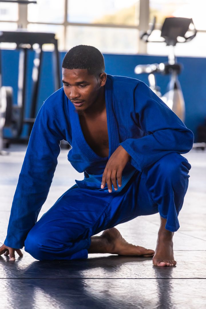 Martial Artist Kneeling in Blue Gi During Training Session in Gym