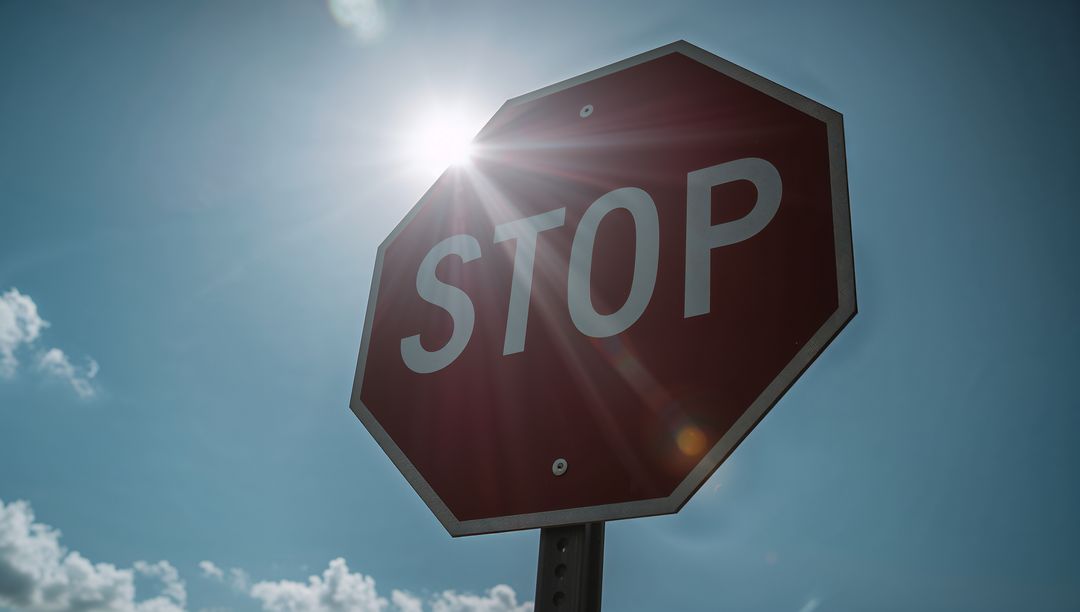 Sun flare streaking across red octagon stop sign with lens flare and bright blue sky