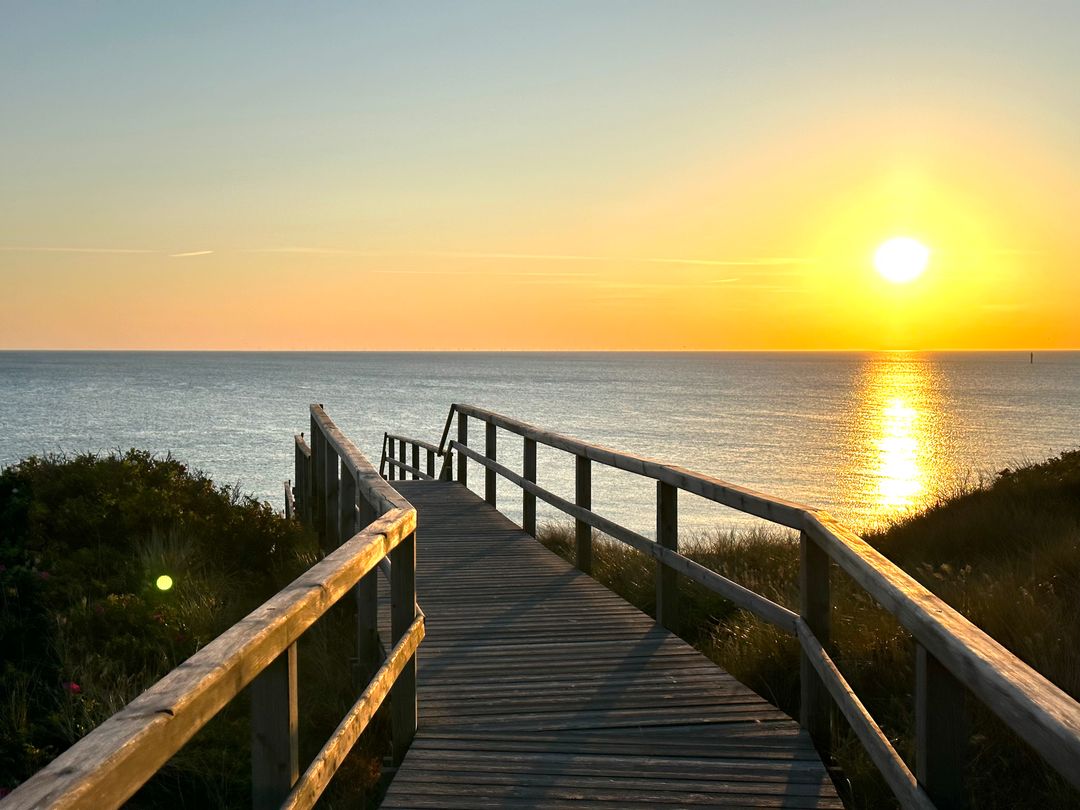 Tranquil boardwalk facing beach sunset over ocean horizon