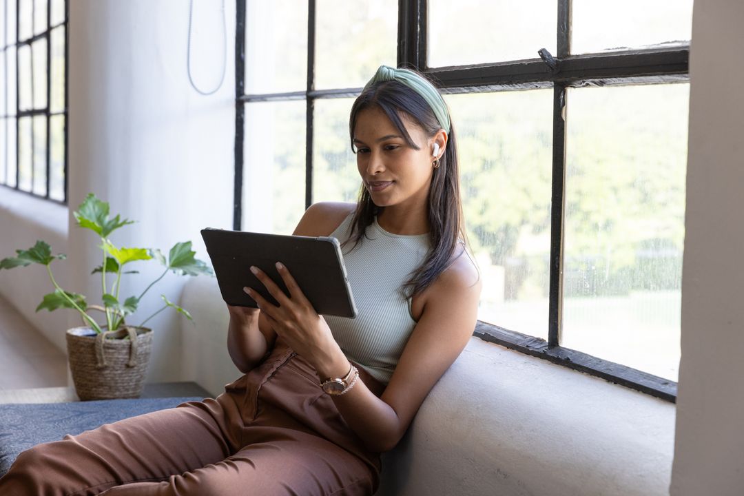 Asian woman using tablet while relaxing by window in modern lounge