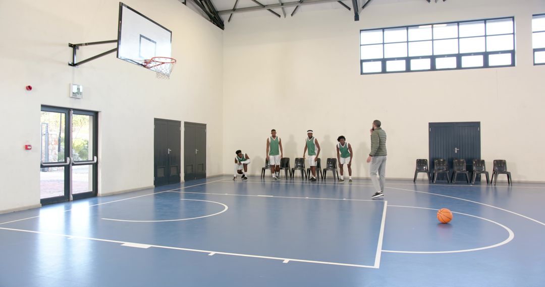 Diverse Basketball Team Training with Coach Using Smartphone in Gymnasium