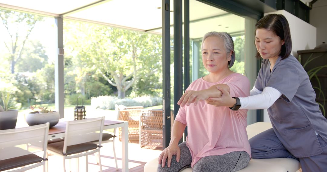 Physiotherapist Assisting Asian Senior with Arm Rehabilitation at Home