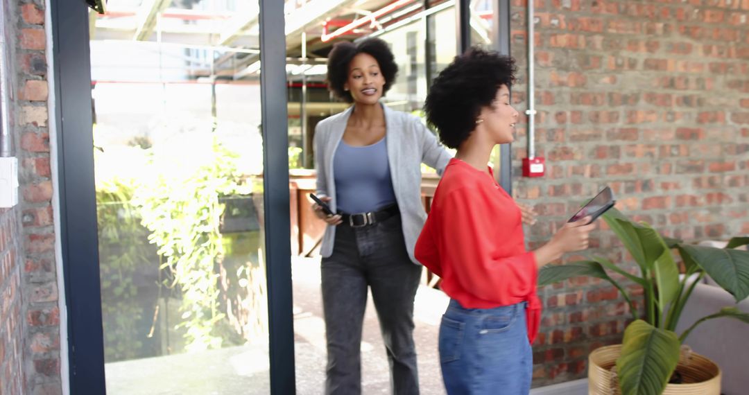 Two colleagues entering modern office talking and holding tablet and phone in entryway