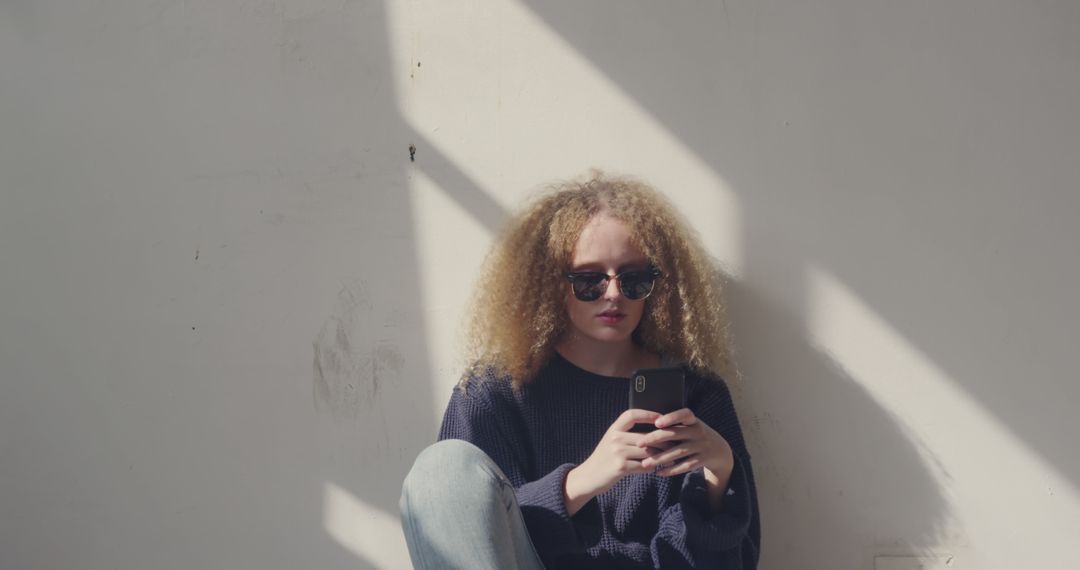 Young Woman with Curly Hair Using Smartphone Against Wall - Free Images, Stock Photos and Pictures on Pikwizard.com