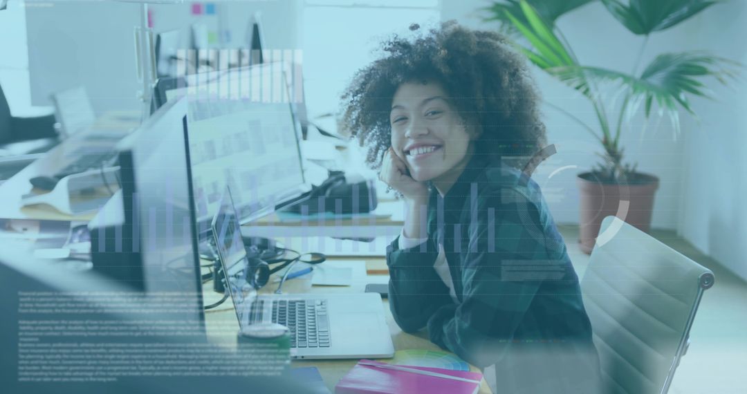 Smiling professional analyzing laptop charts in sunlit open-plan office