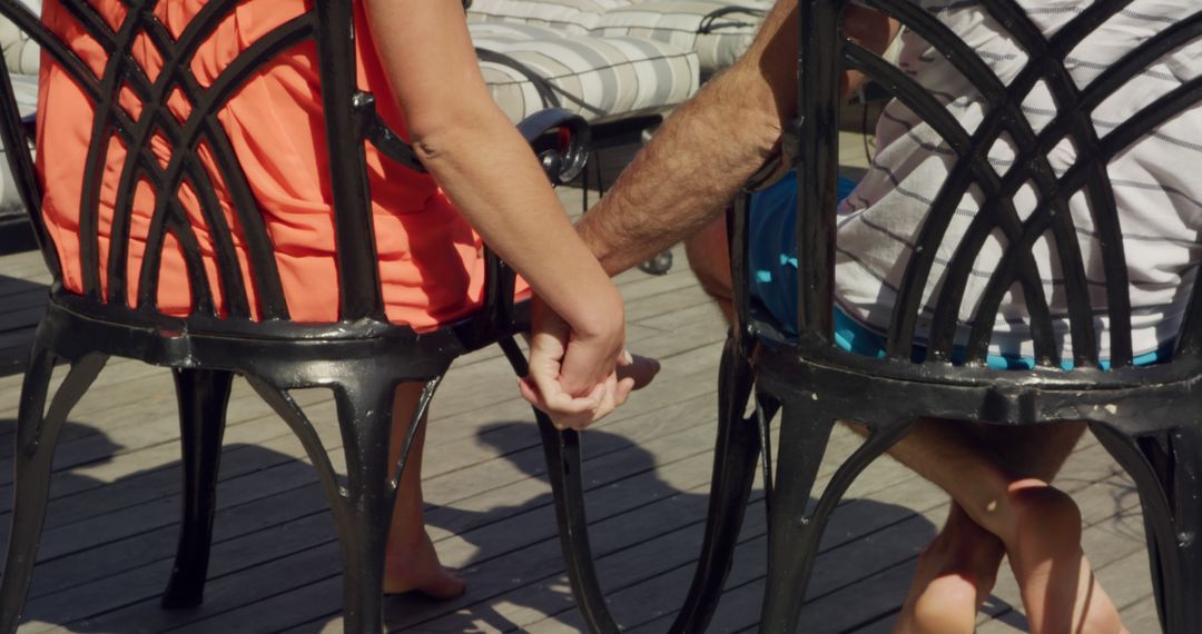 Couple Holding Hands Sitting on Outdoor Chairs at Wooden Deck - Free Images, Stock Photos and Pictures on Pikwizard.com