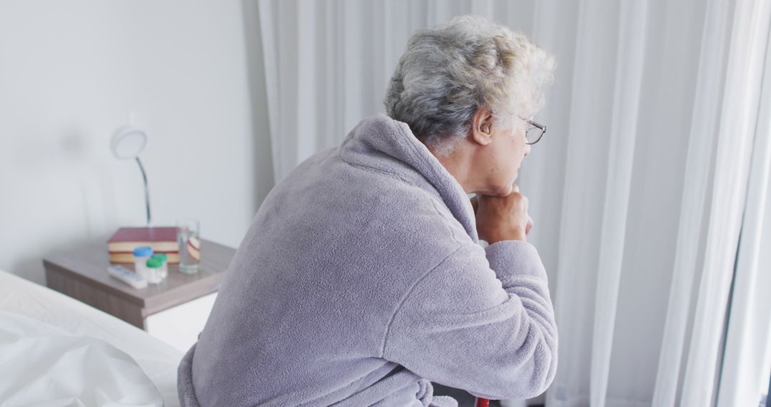 Senior Woman Sitting on Bed Looking Thoughtful by Window in Morning Light - Free Images, Stock Photos and Pictures on Pikwizard.com