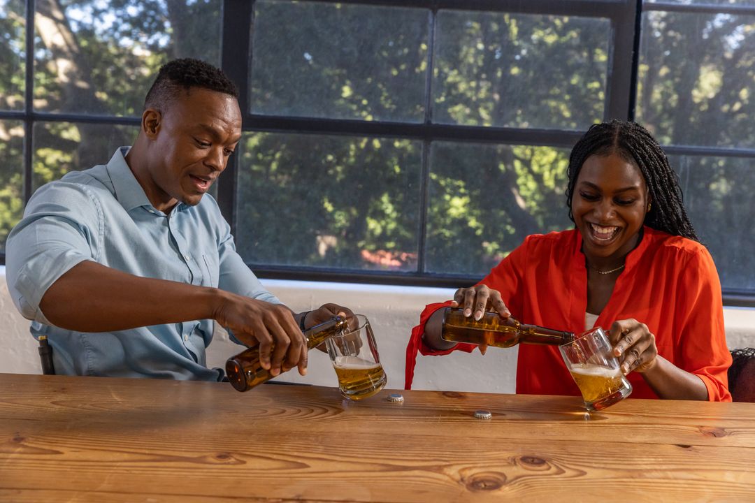 Friends Pouring Beer Enjoying Relaxing Afternoon by Large Window