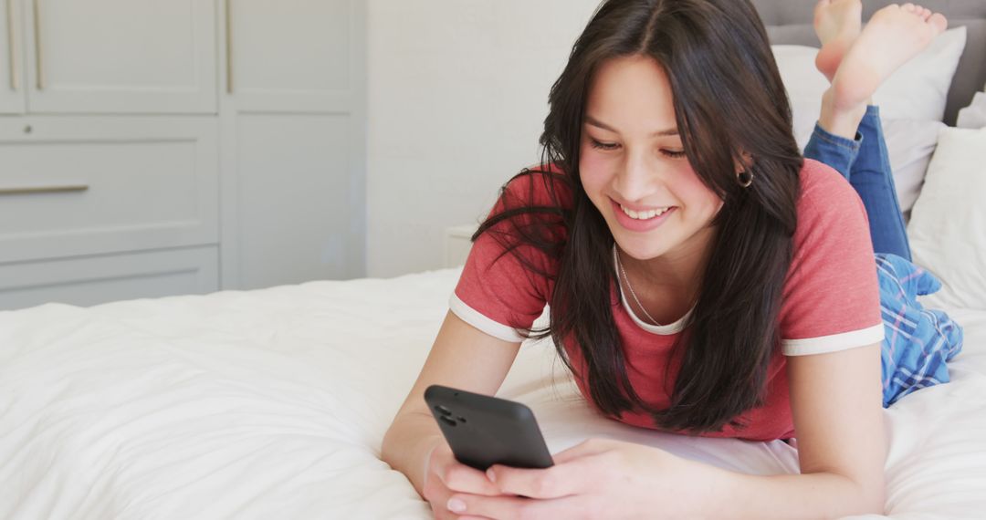 Young Woman Smiling While Using Smartphone on Bed - Free Images, Stock Photos and Pictures on Pikwizard.com