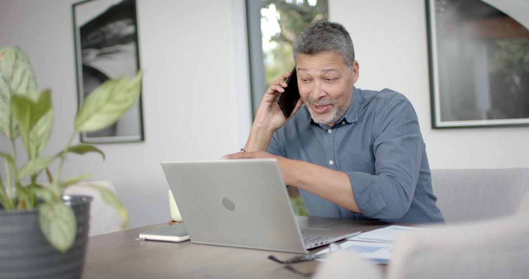 Senior Man Working Remotely using Smartphone and Laptop at Home