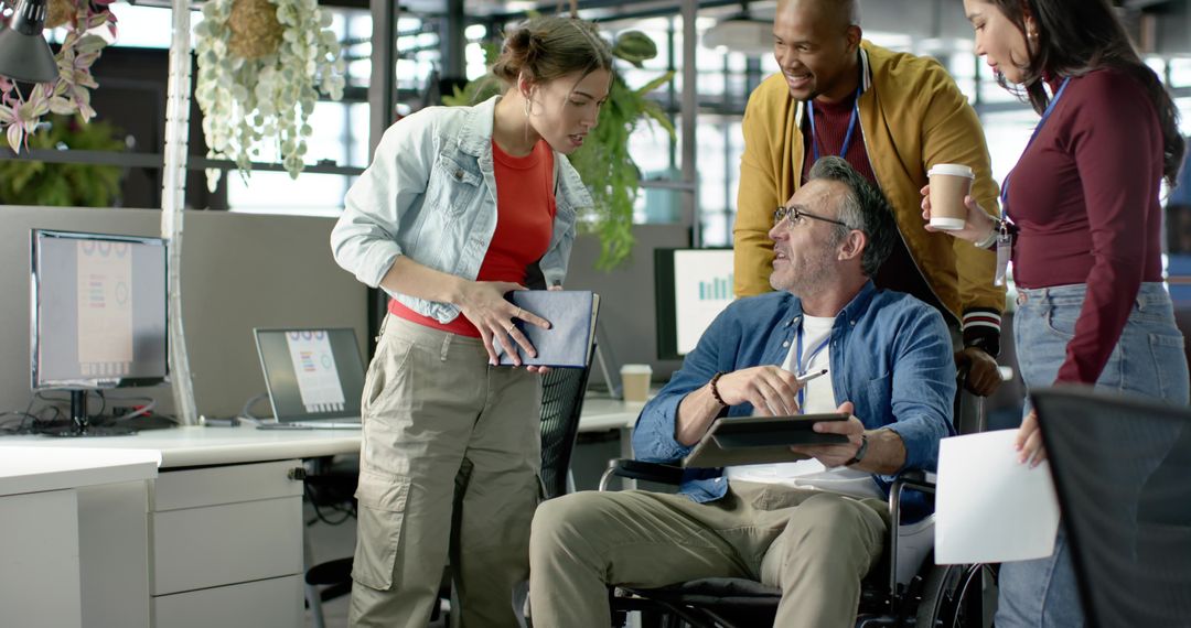 Inclusive office team collaborating with colleague in wheelchair using tablet