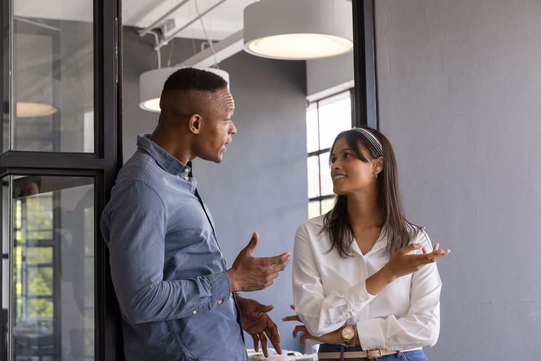 Diverse coworkers discussing project by glass wall in modern office with pendant lights