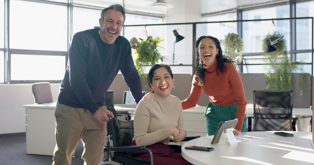 Diverse team supporting colleague in wheelchair, smiling and collaborating in modern office