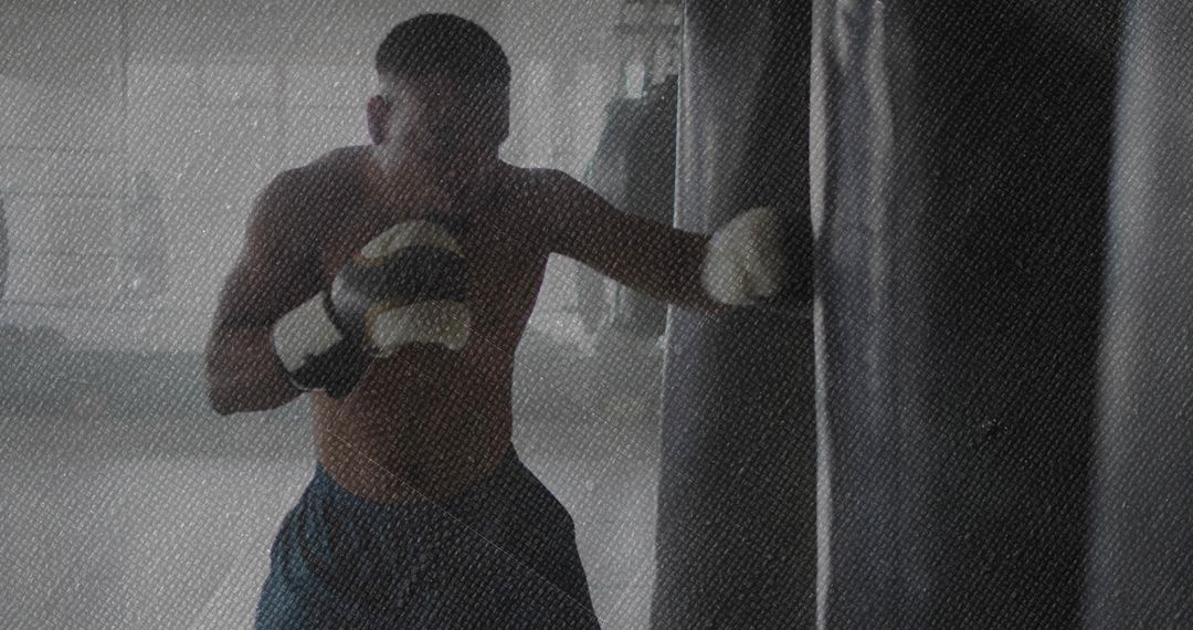Shirtless Backlit Boxer Training on Heavy Bag, Punching with Focus and Strength