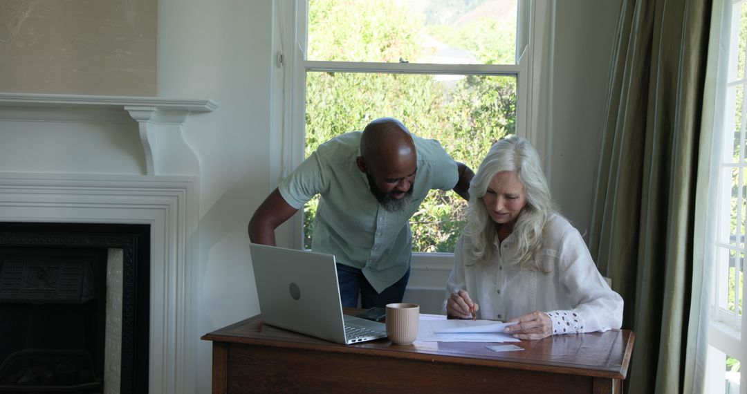 Elderly Couple Reviewing Documents with Laptop at Home