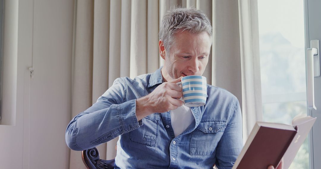 Middle-aged Man Relaxing at Home While Reading Book and Drinking Coffee - Free Images, Stock Photos and Pictures on Pikwizard.com