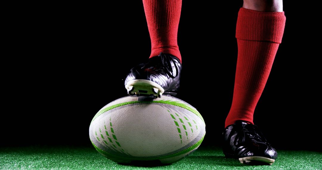 Rugby Player in Red Socks Stands with Foot on Rugby Ball in Low Light - Free Images, Stock Photos and Pictures on Pikwizard.com