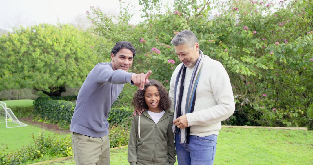 Multiracial fathers pointing with smiling child on garden lawn near youth soccer goal