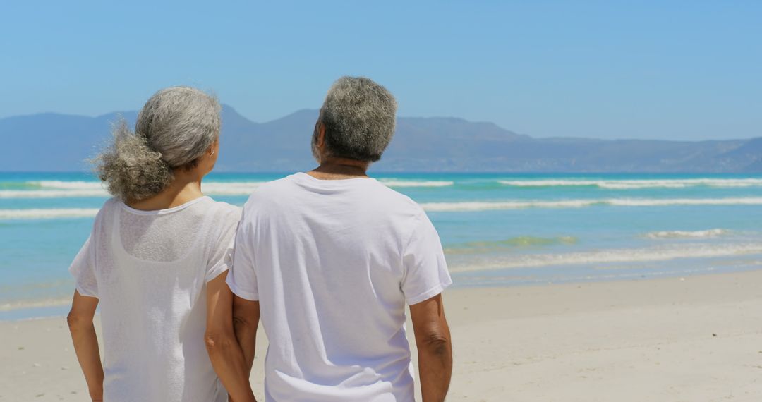 Senior Couple Holding Hands on Beach Looking at Ocean