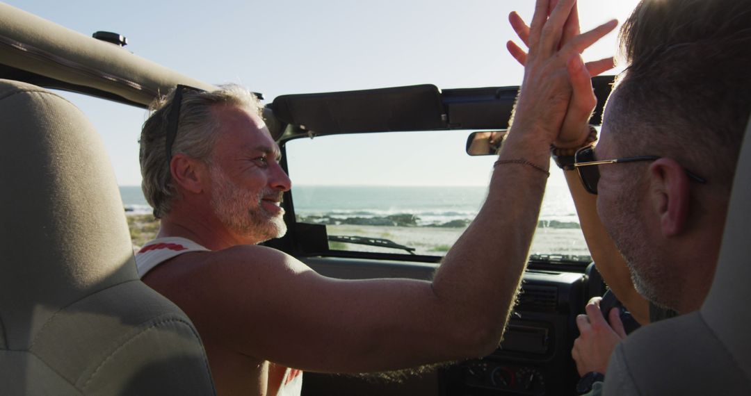 Middle-aged friends high-fiving in convertible by sea on sunny day - Free Images, Stock Photos and Pictures on Pikwizard.com