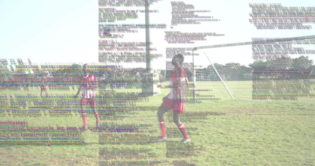 Young Soccer Player Standing by Goal Kicking Ball on Sunlit Field in Red Uniform