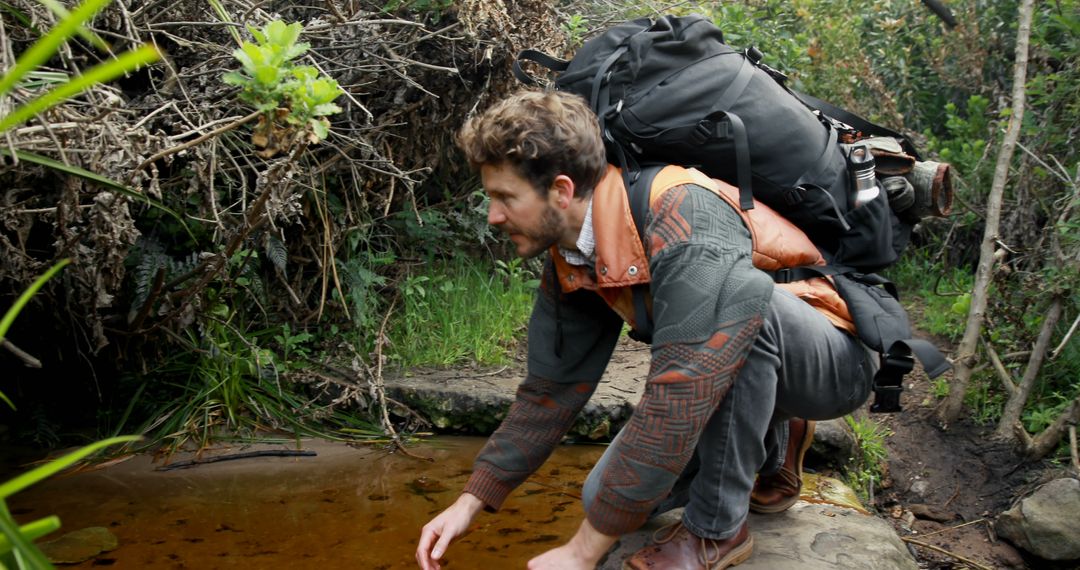 Adventurous Hiker Kneeling at Natural Pond in Forest