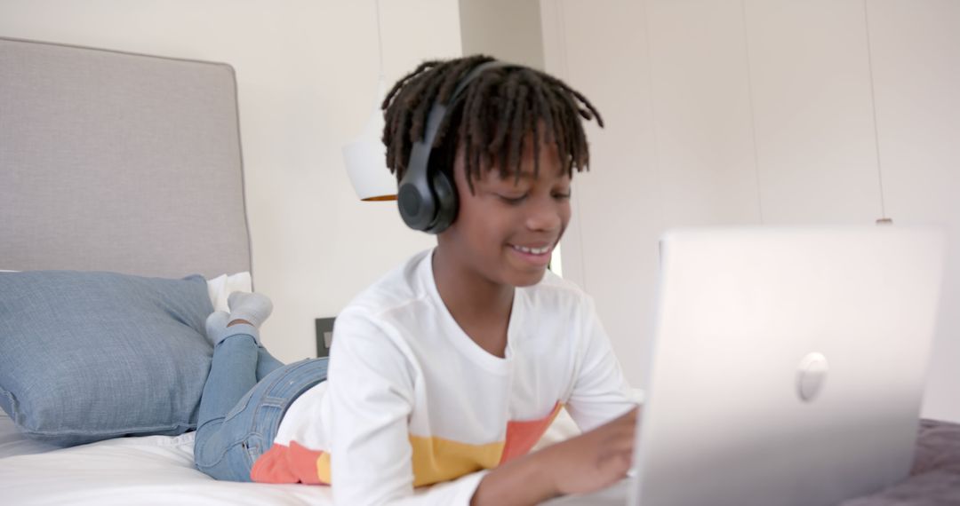 Smiling African American Boy Using Laptop with Headphones on Bed - Free Images, Stock Photos and Pictures on Pikwizard.com