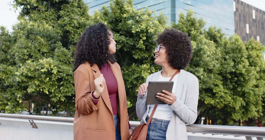 African American women chatting and collaborating on urban walkway with tablet