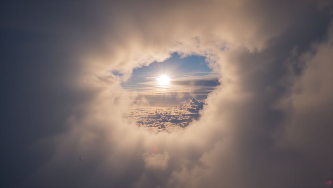 Sun shining through circular cloud opening over golden cloudscape, rays streaming outward