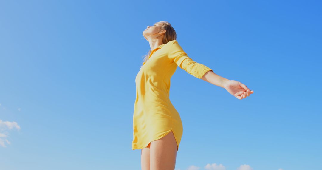 A woman in yellow exudes joy and freedom against a blue sky. - Free Images, Stock Photos and Pictures on Pikwizard.com