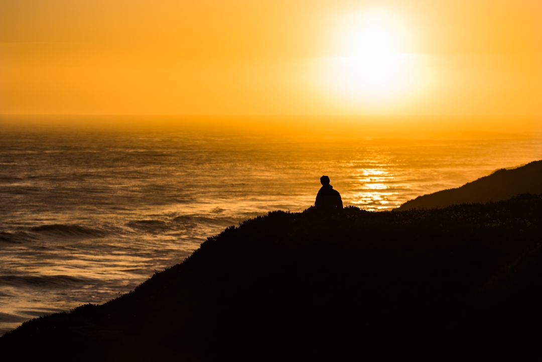 Lone Figure Sits on Clifftop Watching a Beautiful Sunset - Free Images, Stock Photos and Pictures on Pikwizard.com