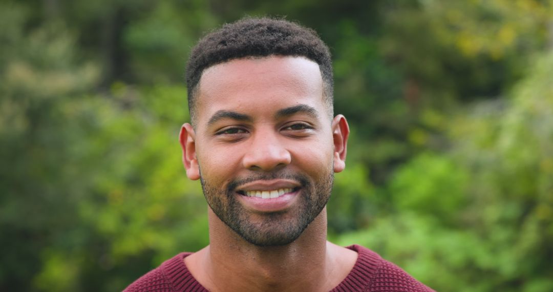 Smiling Man in Maroon Sweater Surrounded by Greenery