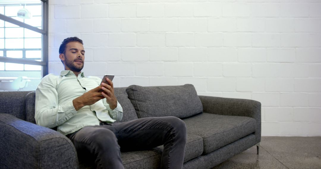 Man Relaxing on Couch Using Smartphone In Modern Living Room - Free Images, Stock Photos and Pictures on Pikwizard.com