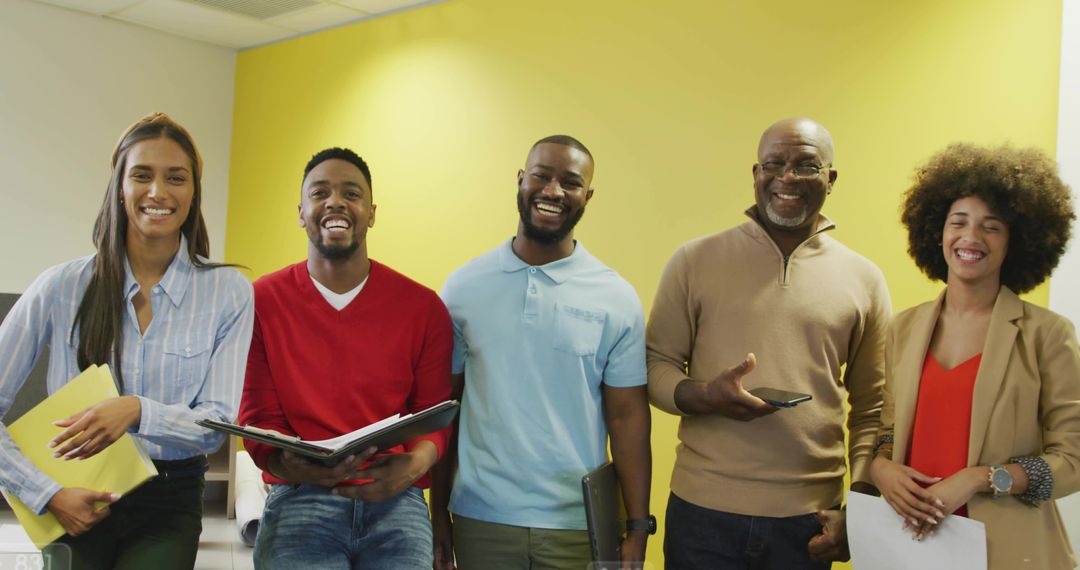 Smiling diverse team standing against yellow wall in modern office workspace