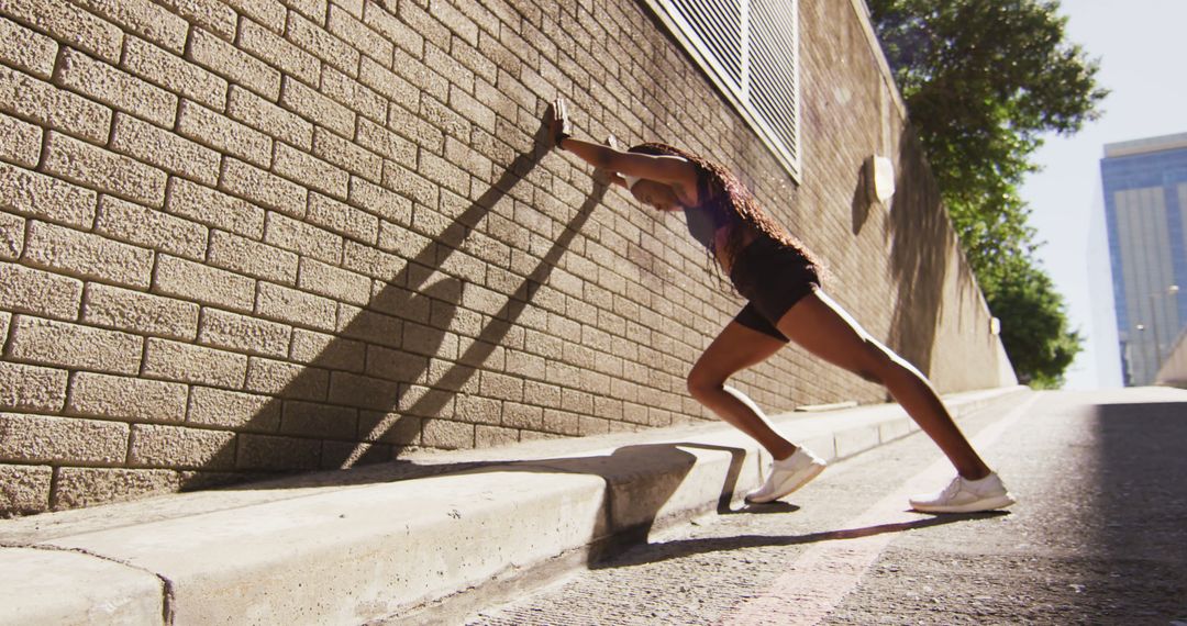 African american woman exercising outdoors leaning of wall and stretching in the city - Free Images, Stock Photos and Pictures on Pikwizard.com