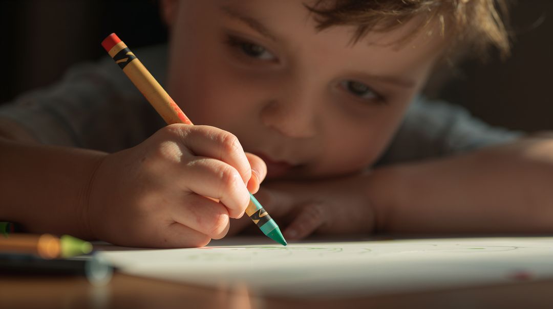 Young Boy Drawing with Green Crayon Close-Up Showing Creative Focus and Fine Motor Skill