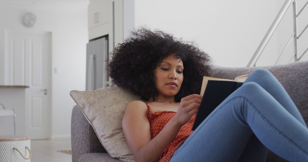 Woman With Curly Hair Relaxing on Sofa Reading Book at Home - Free Images, Stock Photos and Pictures on Pikwizard.com