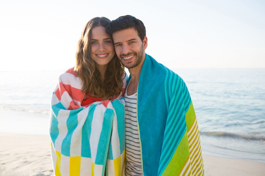 Portrait of happy young couple wrapped in blanket at beach - Free Images, Stock Photos and Pictures on Pikwizard.com