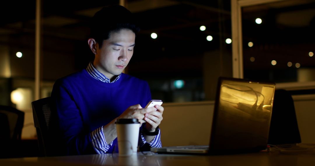 Male Executive Using Smartphone at Desk with Laptop in Office