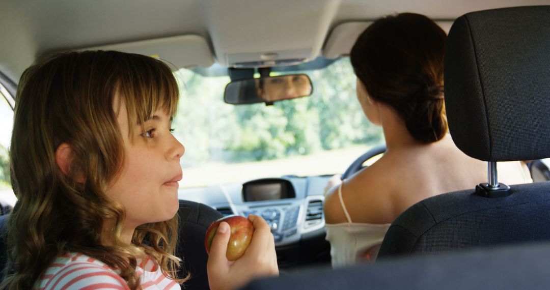 Child Enjoying Apple in Car Backseat with Woman Driver